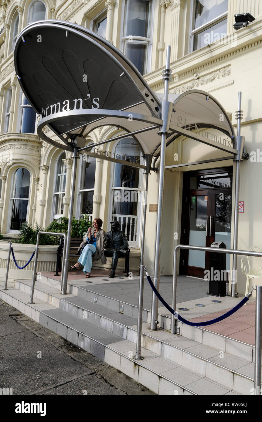 Ein Besucher sitzt neben lebensechten Statue am hotelÕs Eingang sitzen ist eine der Insel der berühmte Bewohner des Menschen, TV und Film Komödie Schauspieler, Sir Stockfoto