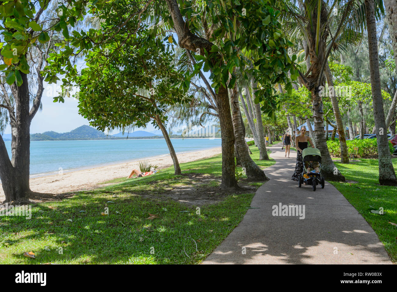 Mutter Schieben eines Kinderwagens auf einem Wanderweg unter verbogen Palmen am Strand entlang, Palm Cove, Far North Queensland, Queensland, FNQ, Australien Stockfoto