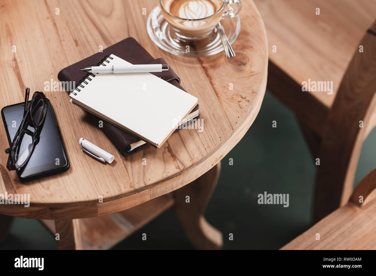 Abstrakte Szene geöffnet kleines Notizbuch, Stift, Brille, Handy, und Kaffee Tasse auf Holz. Kaffeepause und Zeit entspannen. Arbeiten von anywher Stockfoto