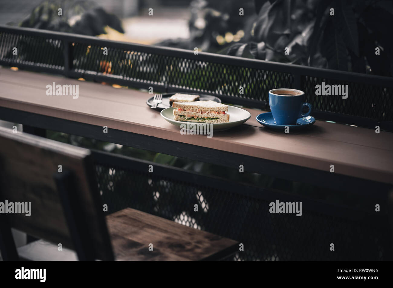 Abstrakte Szene von Frühstück Mahlzeit einschließlich Thunfisch Sandwich, einen langen schwarzen Kaffee und Schokoladenkuchen Käsekuchen auf Holz im Außenbereich bar. Wochenende Morgen Acti Stockfoto