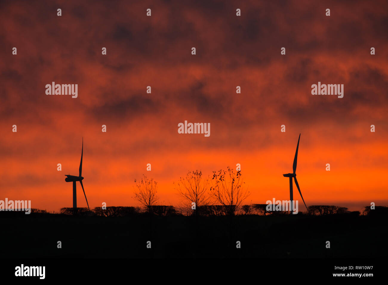 Zwei Windkraftanlagen setzten gegen einen spektakulären roten Abendhimmel Stockfoto