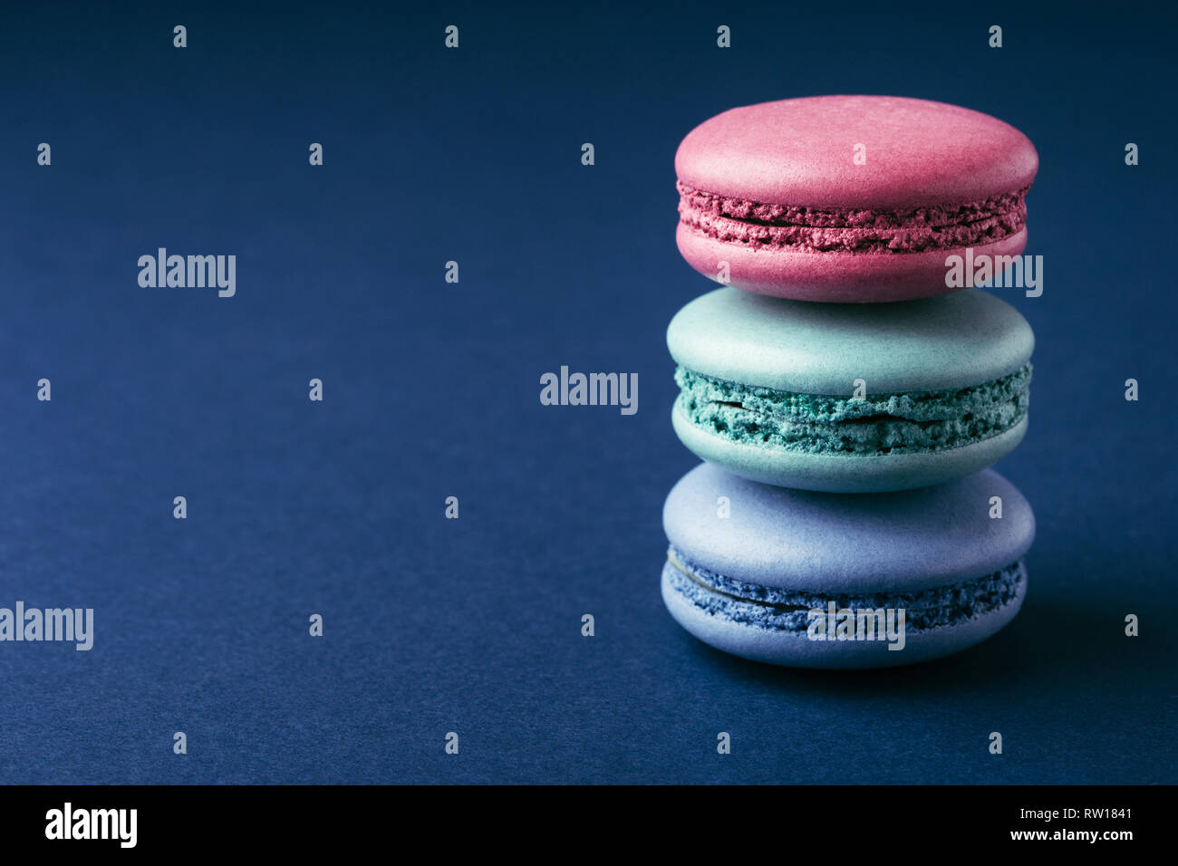 Stapel von drei bunte Macarons auf dunkelblauem Hintergrund mit kopieren. Stockfoto