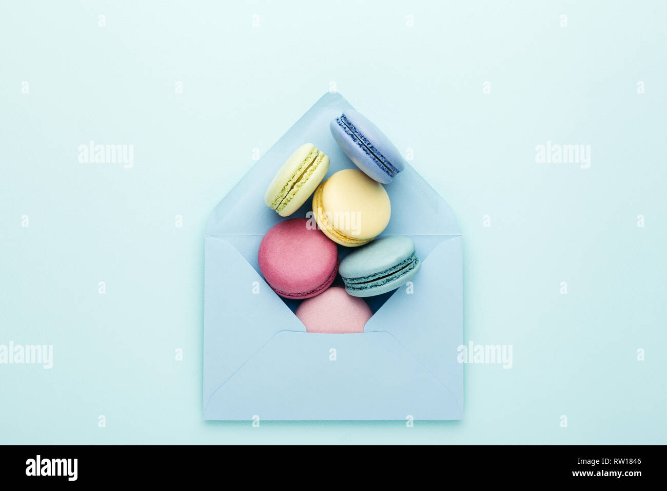 Bunte macarons in blauen Umschlag auf Türkisfarbenem Hintergrund. Ansicht von oben, aus der Nähe. Stockfoto