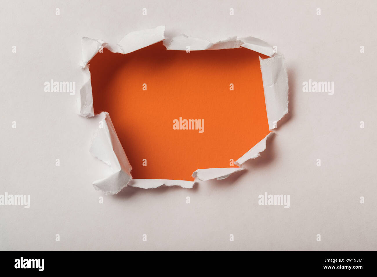 Gerissene Loch in Blatt Papier auf orange Hintergrund Stockfoto