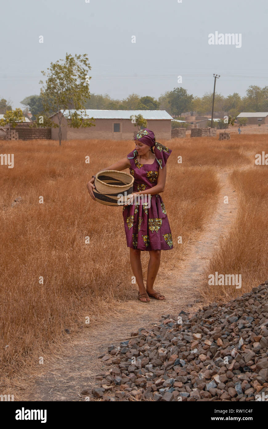 Ein Foto von einer schönen kaukasischen Frau trägt ein lila traditionellen ghanaischen Kleid posiert für die Kamera mit einem berühmten Korb Bolga. Stockfoto