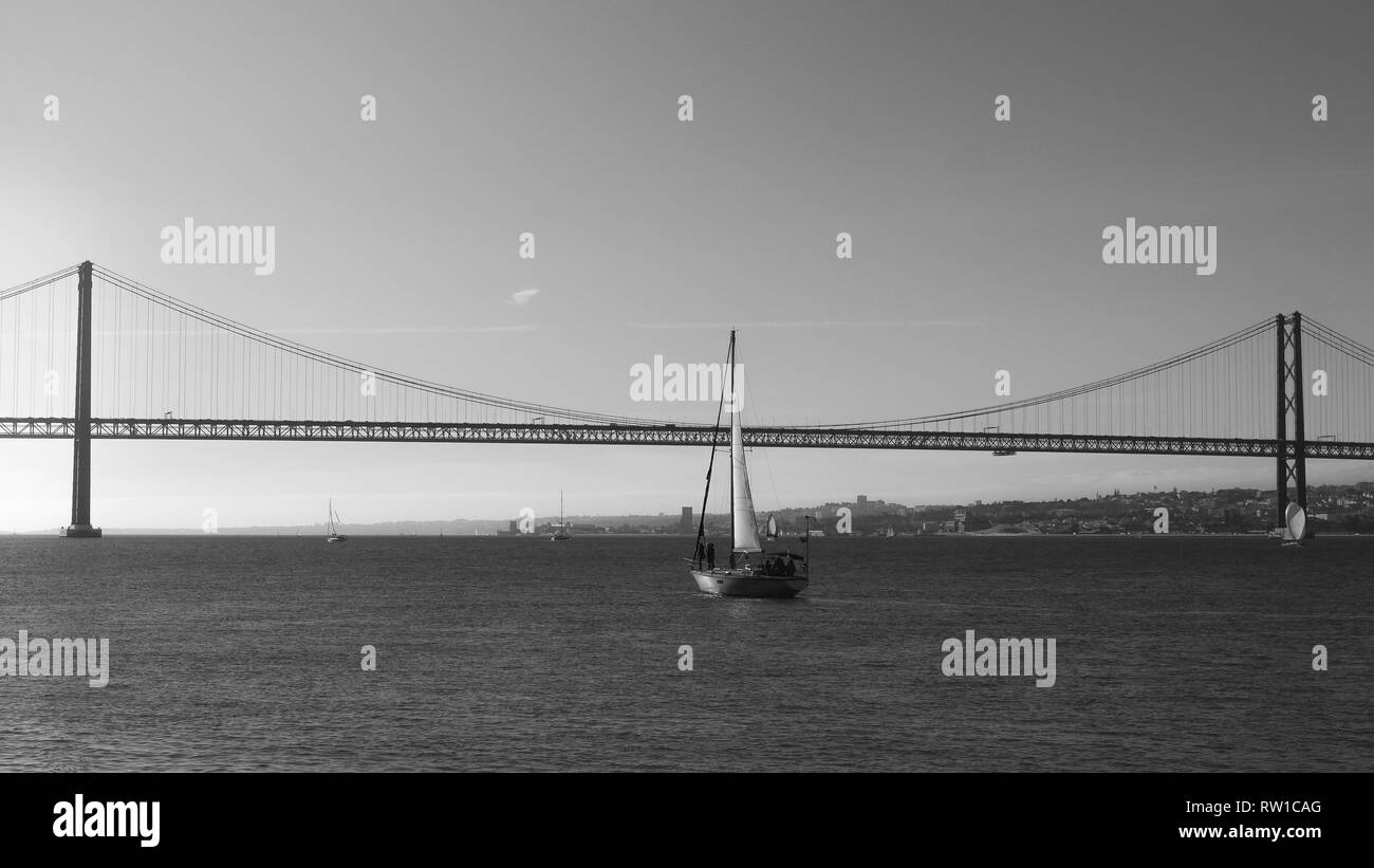 Segelboote mit weissen Segeln auf den Tejo, den 25. April Brücke, Lissabon, Portugal - Monochrom. Stockfoto