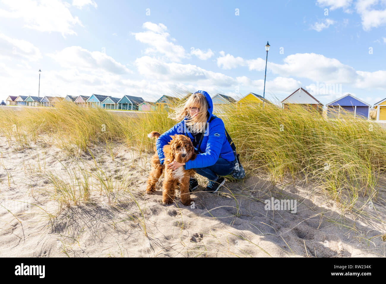 Sutton on Sea, Lincolnshire, Großbritannien. März 2019. UK Wetter: 04/03/19 Hell, sonnig, aber sehr windig Tag Größen Hund Walker Lesley Thompson und Cockapoo Dexter auf den Sanddünen von Sutton on Sea, Lincolnshire, Ostküste, UK England. Windig, Wolken bilden sich über den Chalets entlang der Küste Kredit: Tommy (Louth)/Alamy Live News Stockfoto