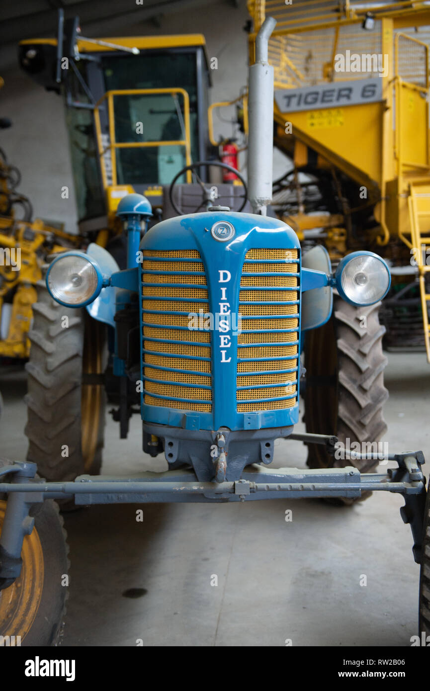 Vorderansicht des blauen Dieseltraktors mit verschiedenen anderen landwirtschaftlichen Geräten dahinter, Broniewo, Woiwodschaft Kujawien-Pommern, Polen Stockfoto