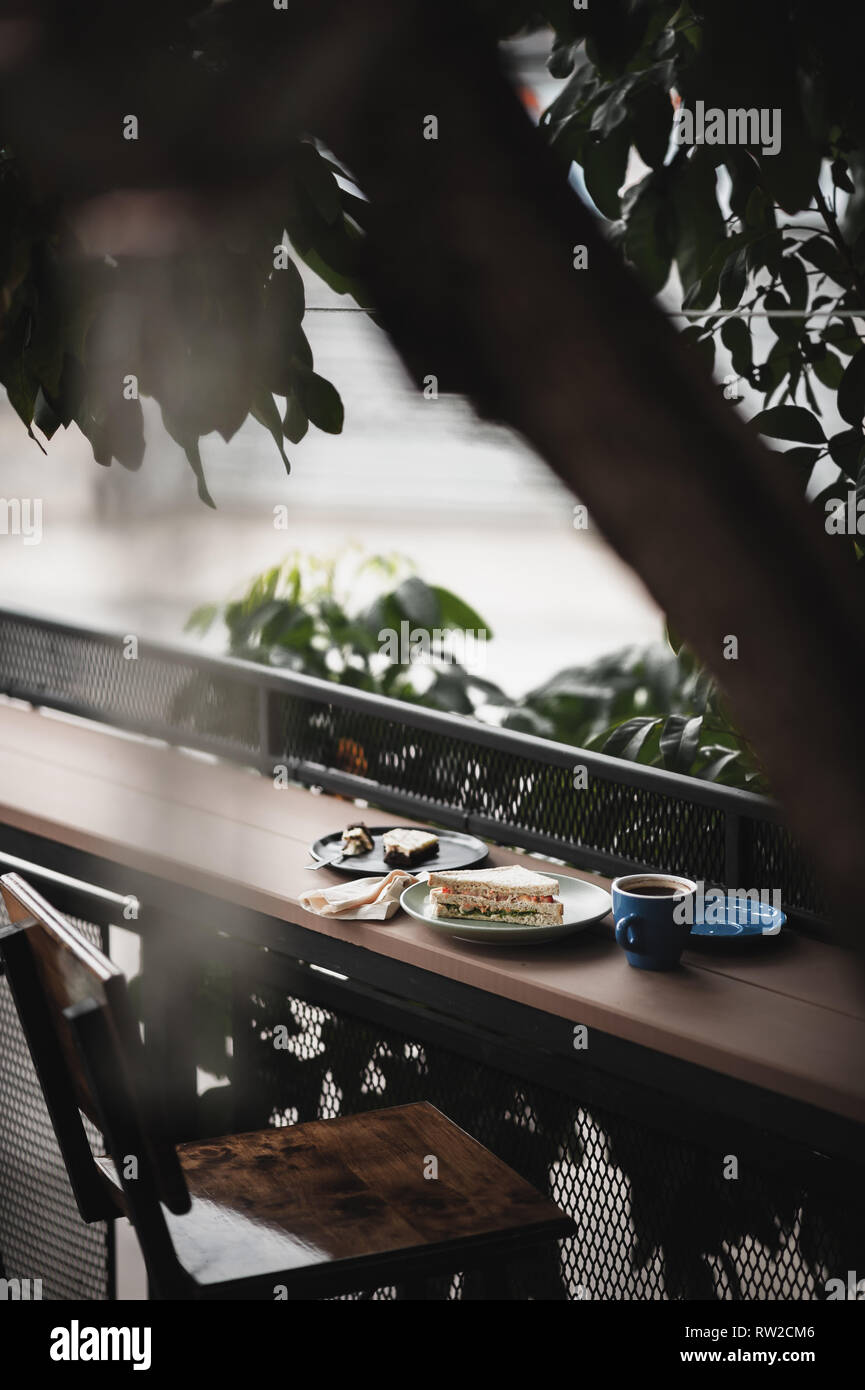 Abstrakte Szene von Frühstück Mahlzeit einschließlich Thunfisch Sandwich, einen langen schwarzen Kaffee und Schokoladenkuchen Käsekuchen auf Holz im Außenbereich bar. Wochenende Morgen Acti Stockfoto