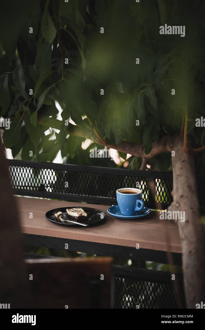 Abstrakte Szene der Kaffeepause Mahlzeit inklusive Set schwarz Kaffee und Schokoladenkuchen Käsekuchen auf Holz im Außenbereich bar. Wochenende Morgen Aktivität mit guten emotio Stockfoto