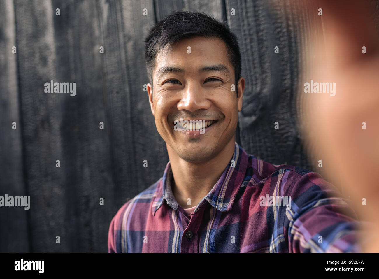 Lächelnden jungen asiatischer Mann lehnte sich gegen eine Wand selfies unter Stockfoto