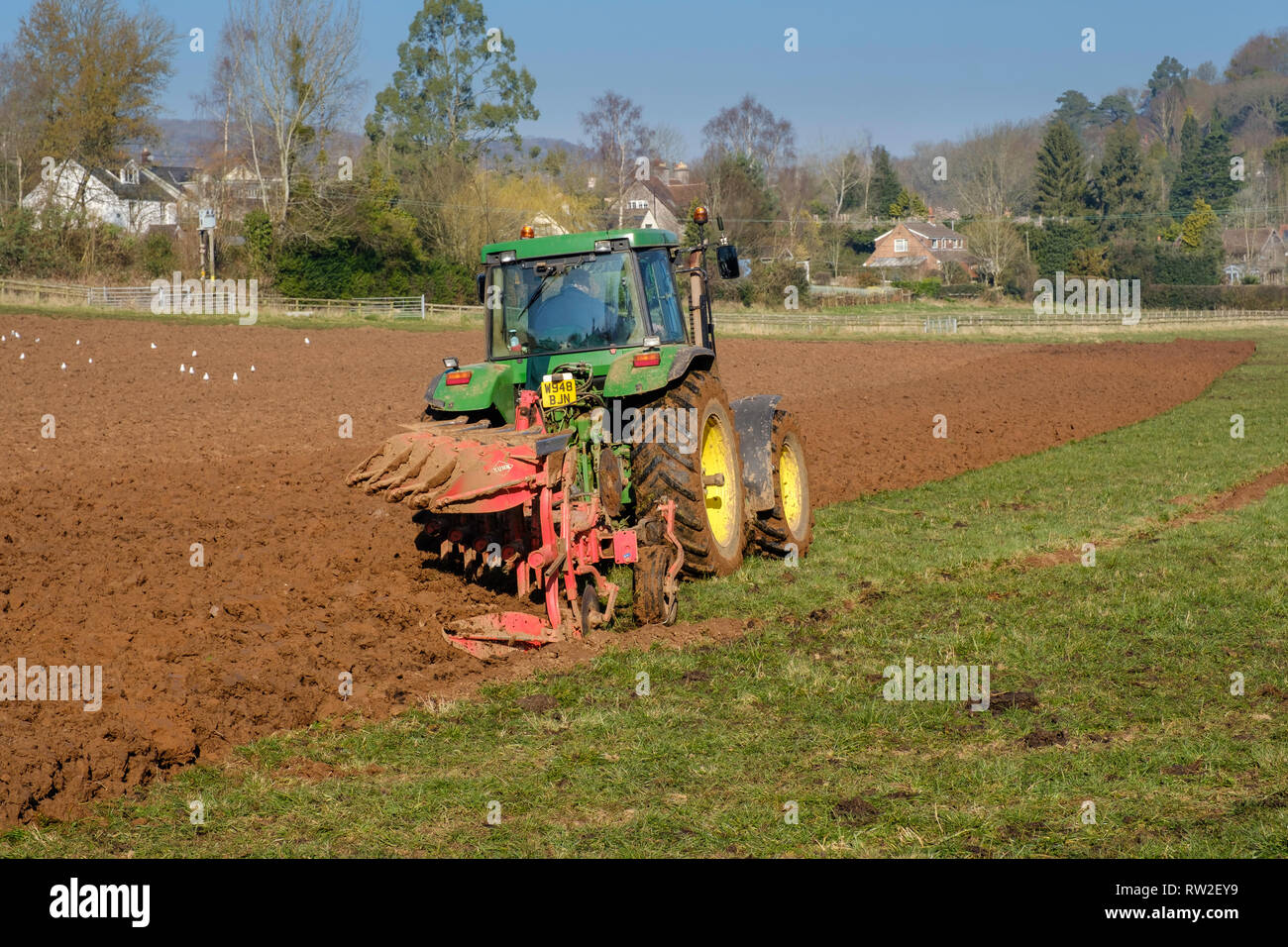 Frühling Pflügen MIT GRÜNEN TRAKTOR IM FELD IN Gloucestershire, England, Großbritannien Stockfoto