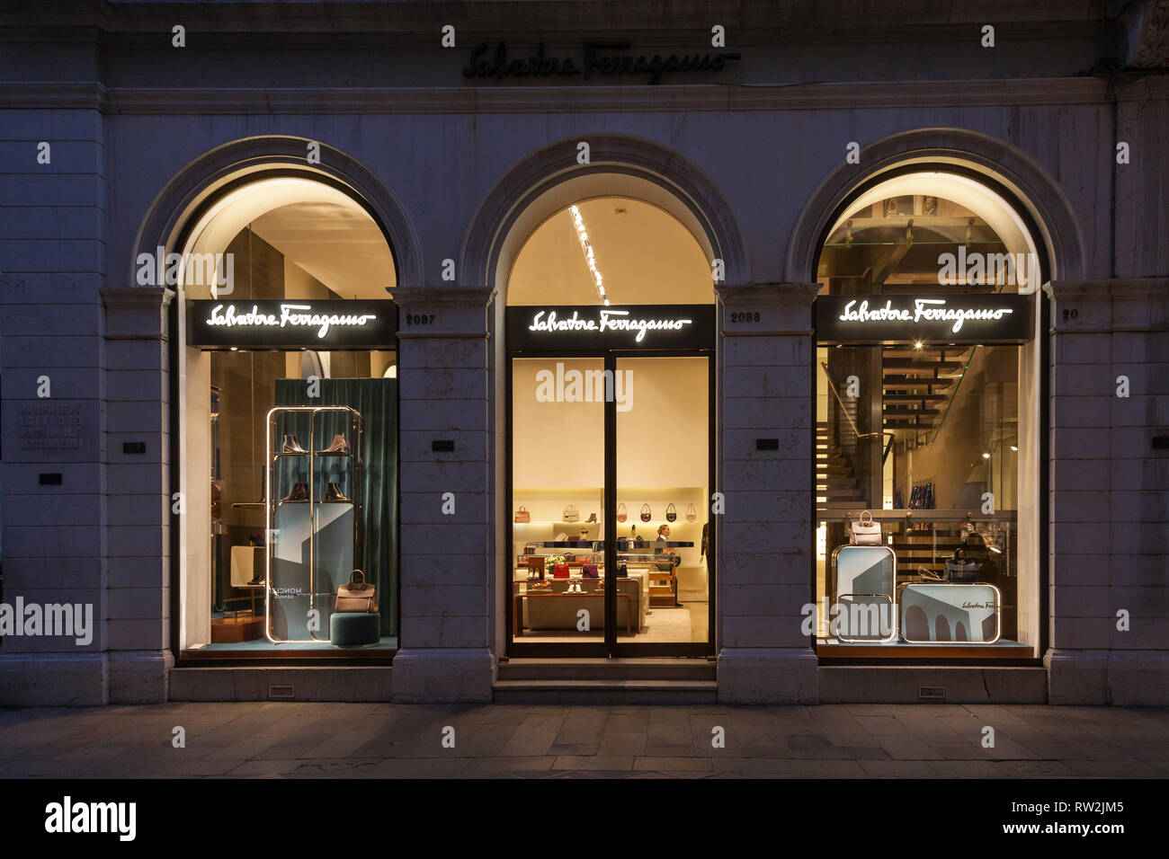 Salvatore Ferragamo Einzelhandelsgeschäft in der Calle Larga XXII Marzo, San Marco, Venedig, Venetien, Italien in der Nacht mit signage beleuchtet. Shop Assistant innen Stockfoto