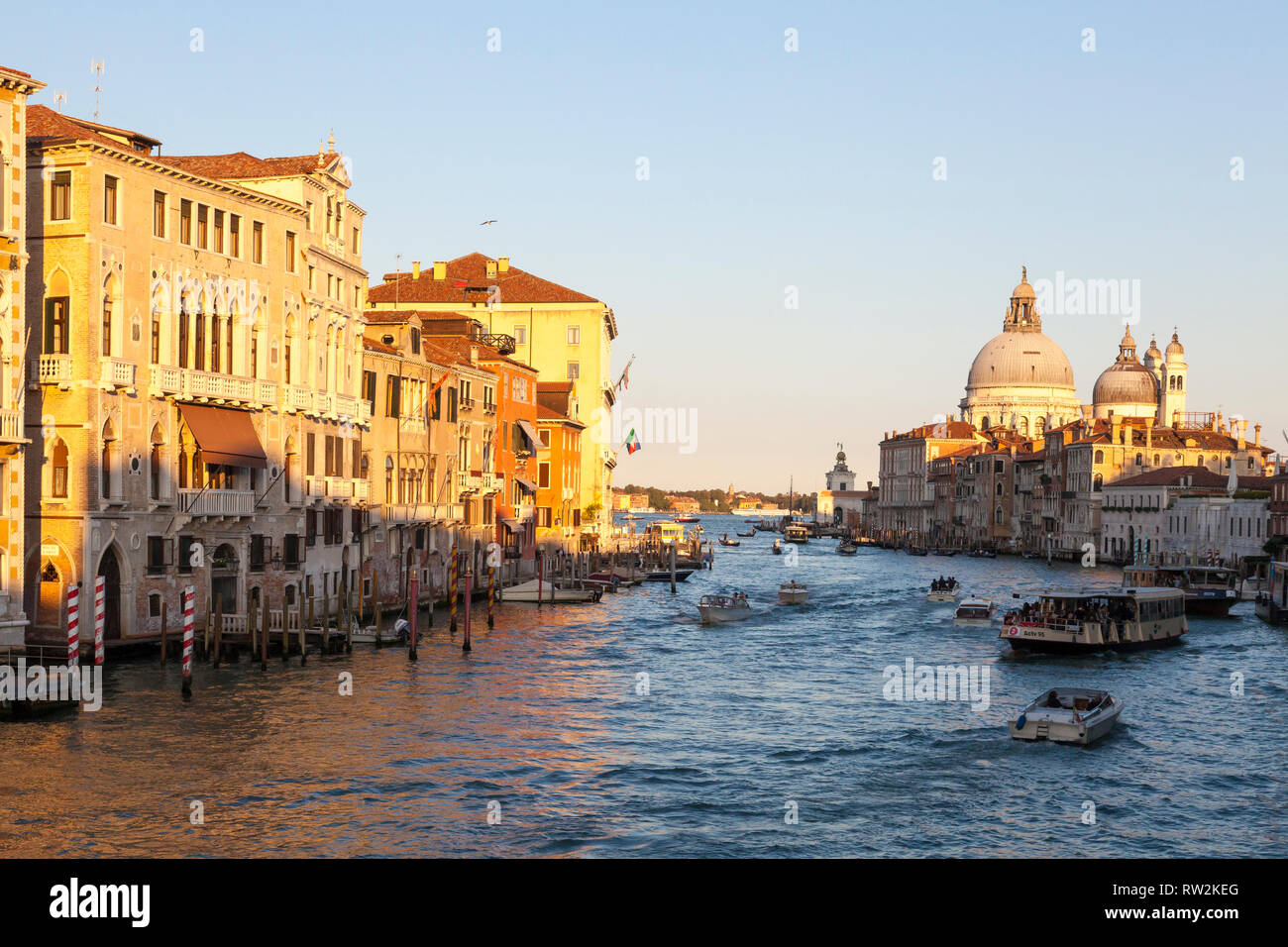 Golden Sunset am Grand Canal und der Basilika di Santa Maria della Salute, Venedig, Venetien, Italien mit Schiffsverkehr und Reflexionen auf dem Wasser Stockfoto