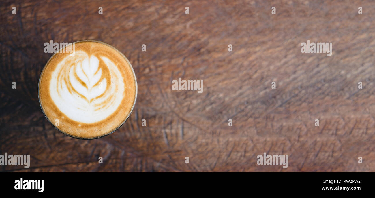 Blick von oben auf die heißen Cappuccino Tasse auf Holz- Fach mit latte Kunst auf Holz Tisch im Cafe, Banner Größe Essen und Trinken Konzept. Kopieren sie Raum lassen für Addi Stockfoto