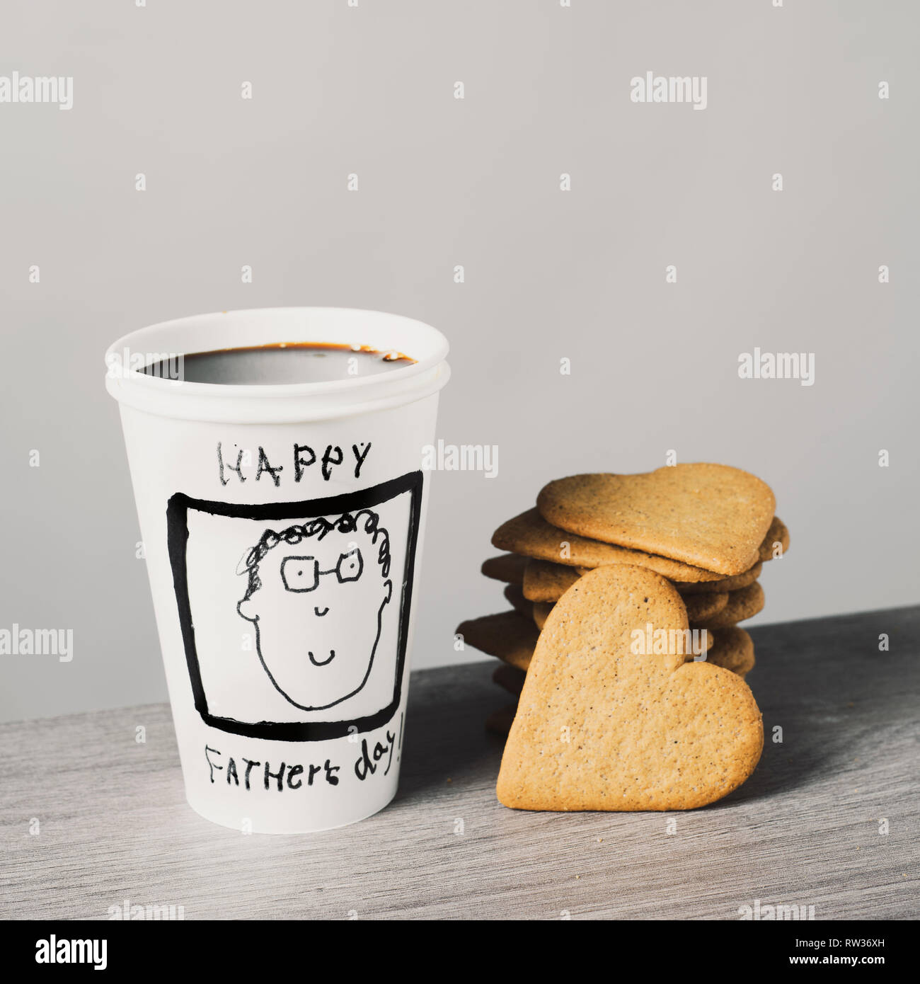 Nahaufnahme von einem verwerfbaren Tasse mit Kaffee, mit dem Text happy Vatertag handschriftlich in es, und einige herzförmige Plätzchen auf einem Tisch Stockfoto