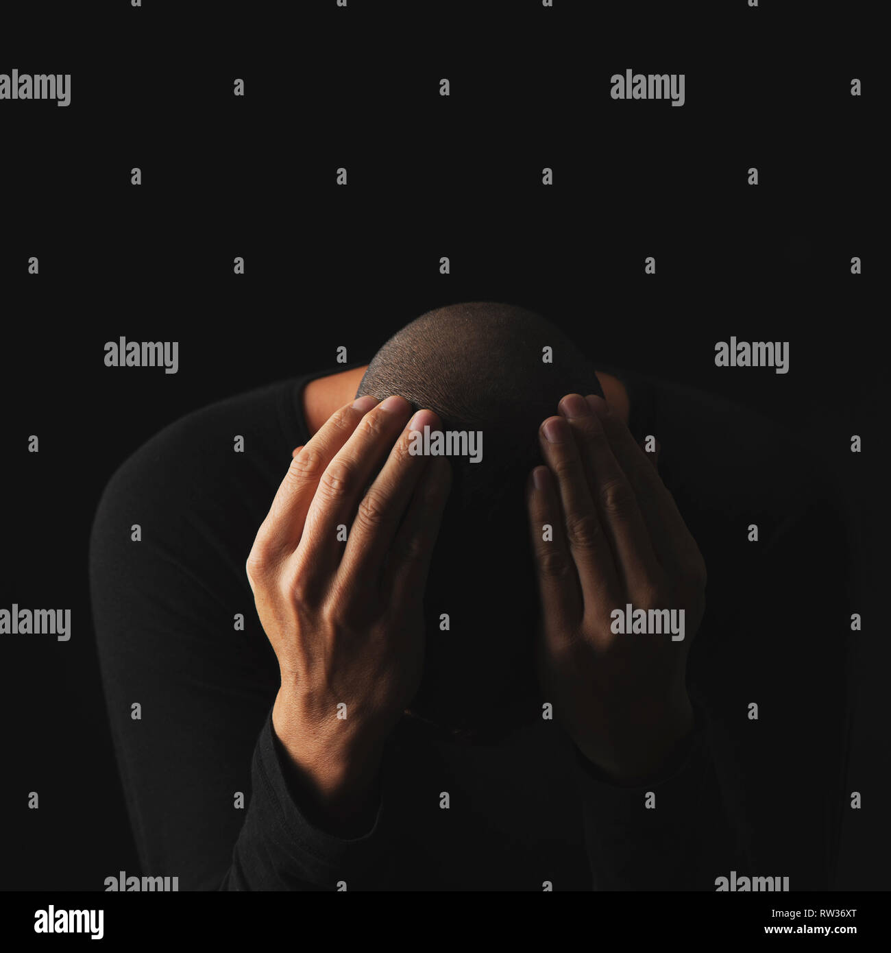 Nahaufnahme eines verzweifelten jungen kaukasischen Mann mit seinen Händen in seinen Kopf, vor einem schwarzen Hintergrund Stockfoto