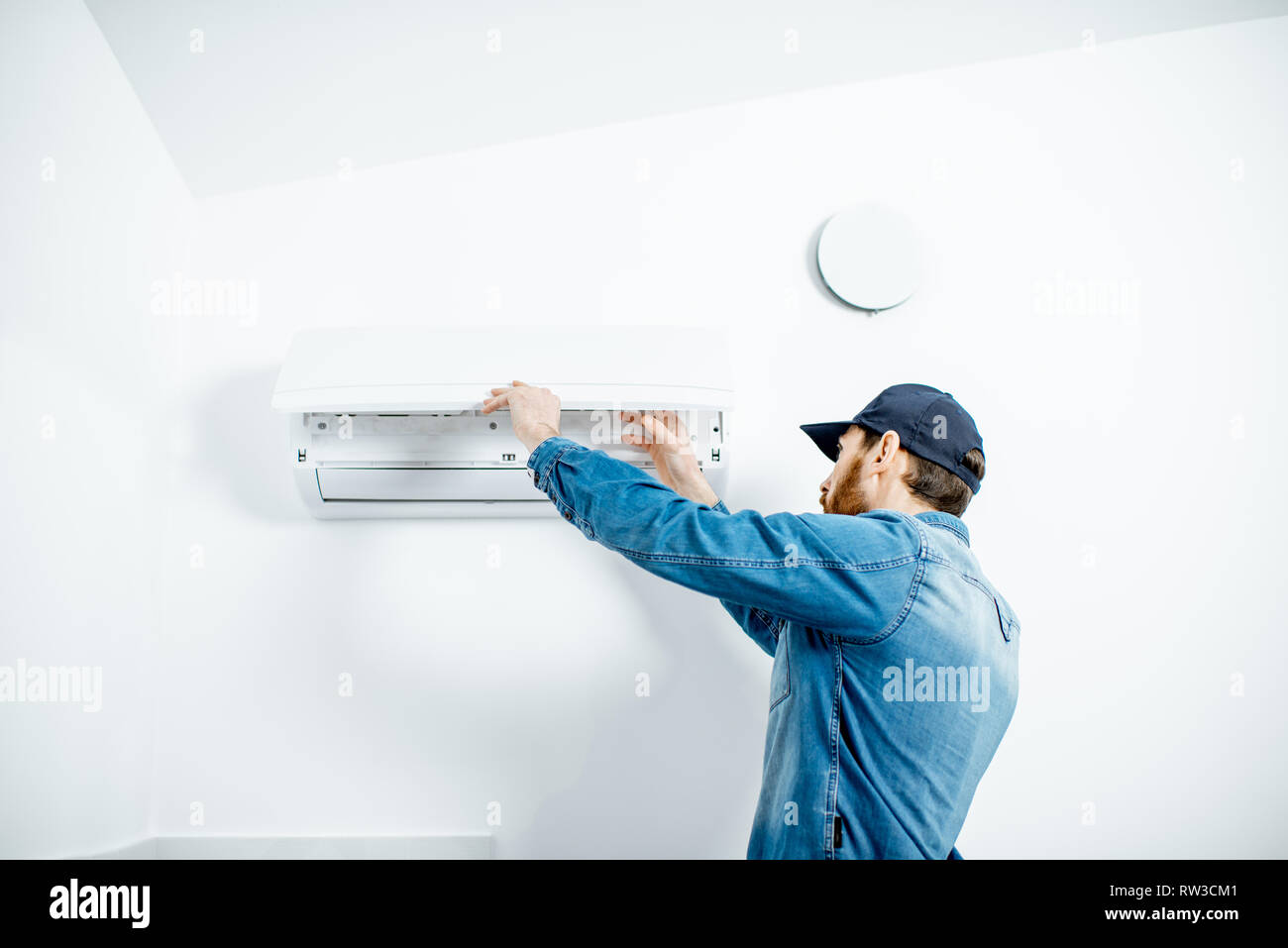 Handwerker in blauer Arbeitskleidung, die Klimaanlage Filter auf der weißen Wand Hintergrund Stockfoto