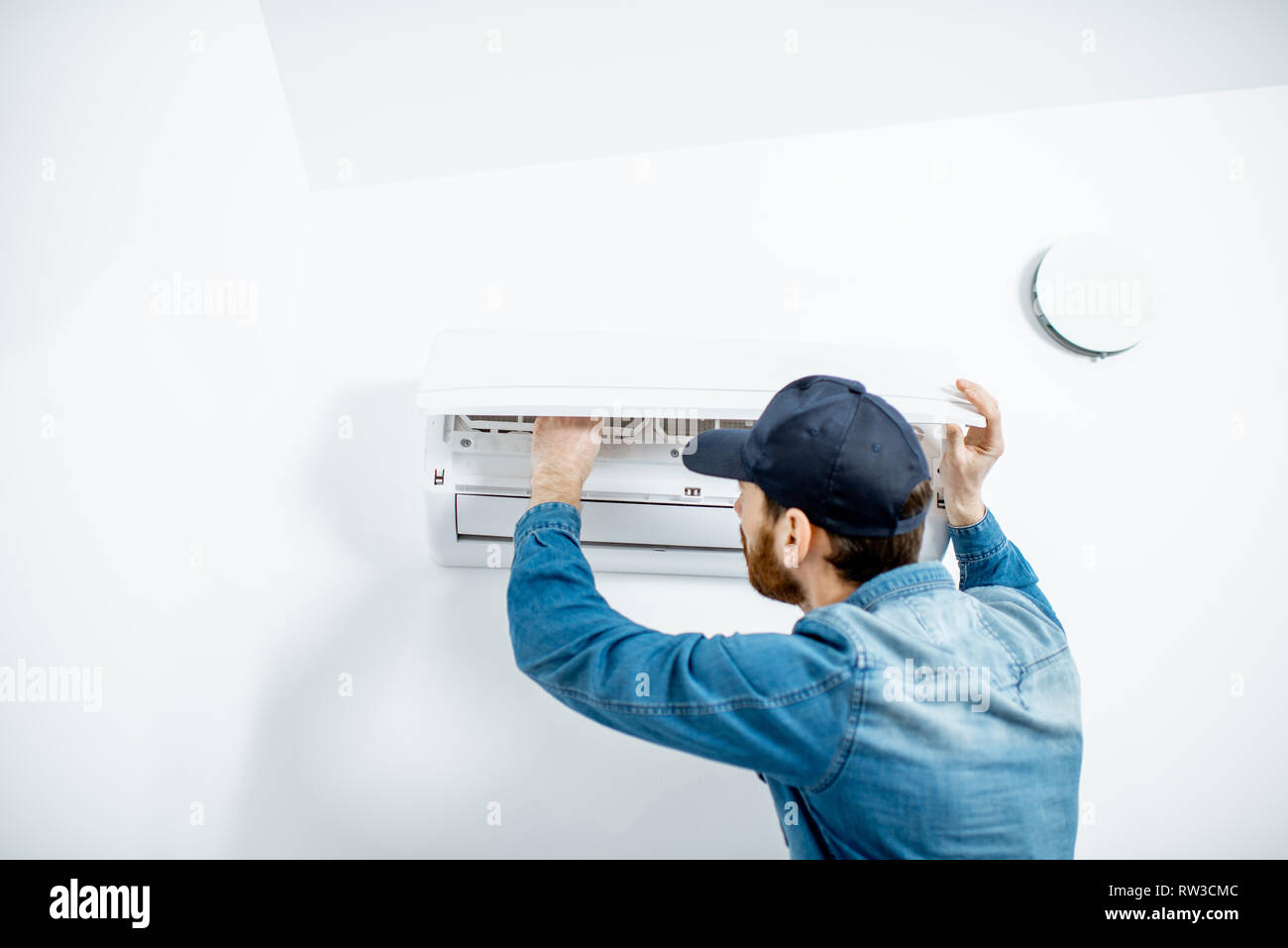 Handwerker in blauer Arbeitskleidung, die Klimaanlage Filter auf der weißen Wand Hintergrund Stockfoto