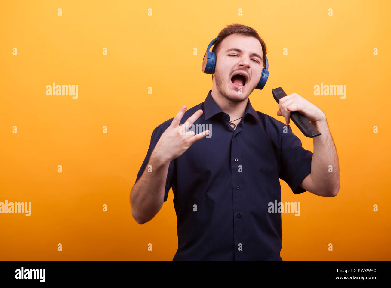 Hübscher junger Mann singen Rockmusik mit seine Kopfhörer auf gelben Hintergrund. Tolle Musik Stockfoto