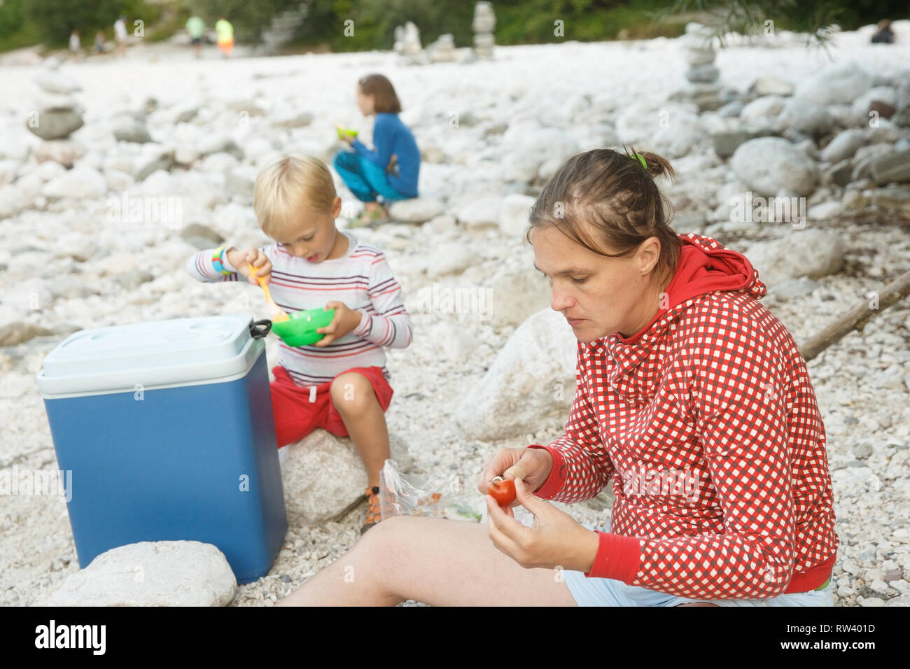 Familie bei einem Picknick in der Natur aus einer Kühlbox, Spaß sitzen auf den Felsen am Ufer. Lebensstil im Freien, positive Parenting, childhoo Stockfoto