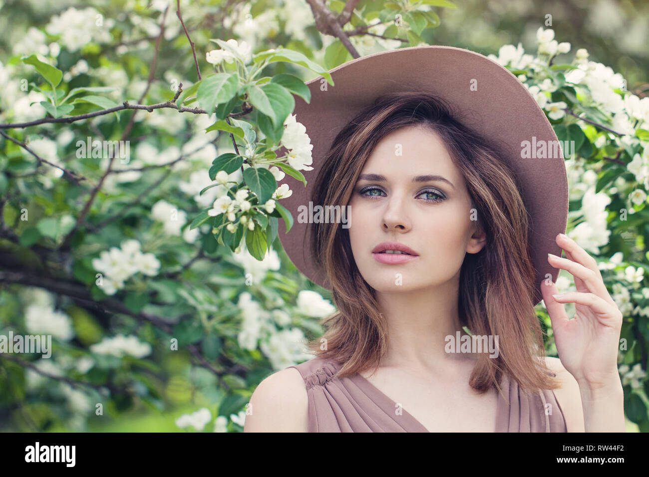 Lebensstil im Freien Foto der jungen Frau. Braune Haare, fedora Hut. Perfekte Gesicht auf Blüten Blumen Hintergrund Stockfoto