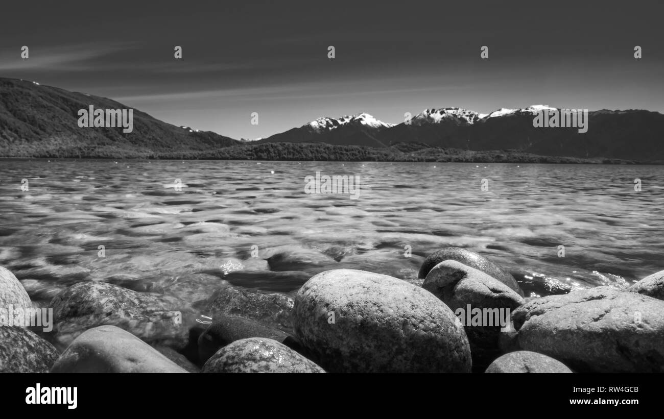 Monochrome steinigen Seeufer des Lake Te Anau Milford von Bergen umgeben Stockfoto