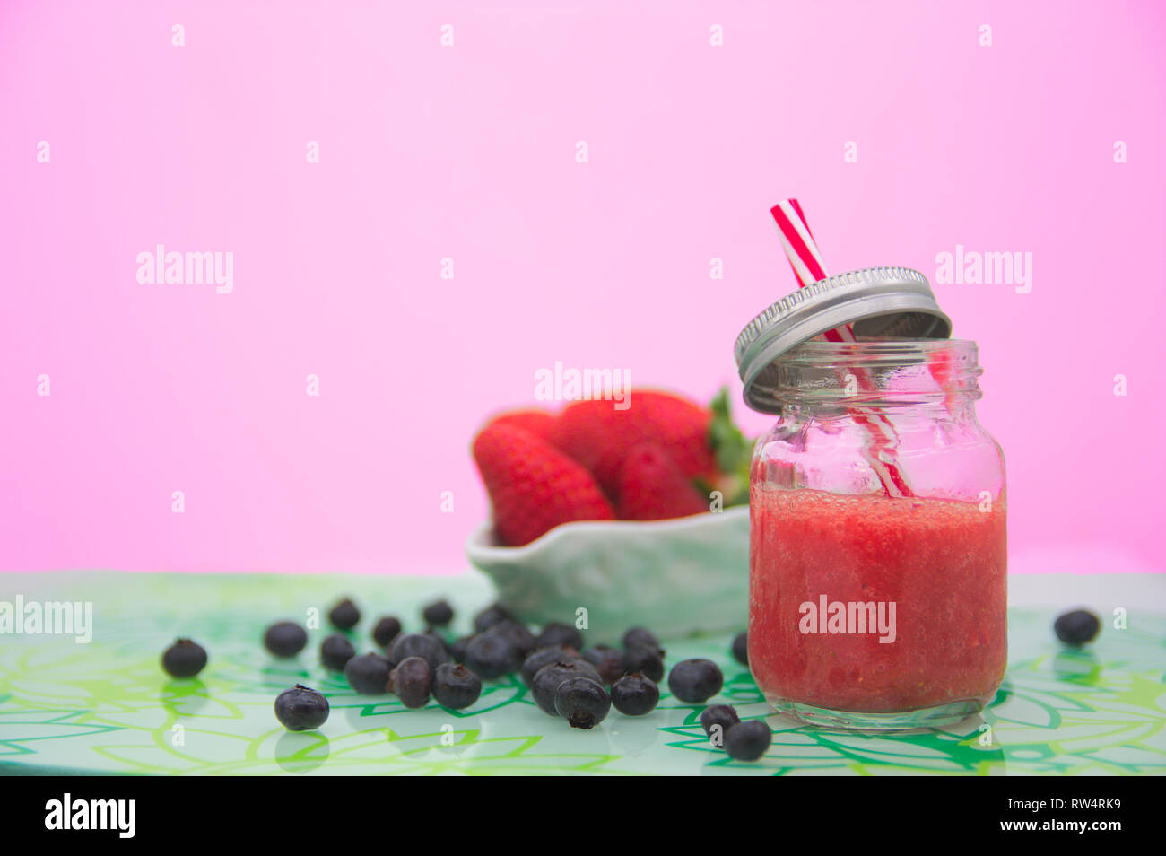 Ein Saft der frischen Erdbeeren in einem Glas neben einigen Blaubeeren und Erdbeeren. Die rosa Hintergrund mit Leerzeichen hinzuzufügen Texte (Kopie) Stockfoto