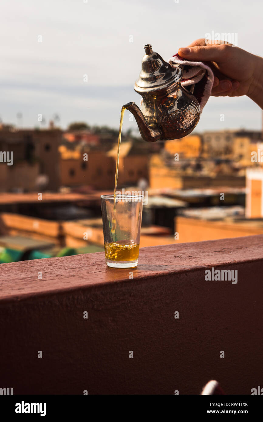 Gießen Typische marokkanische Minze Tee aus einem silbernen karraffe in ein Kaffee Glas über die Dächer der Medina von Marrakesch (Marrakesch, Marokko, Afrika) Stockfoto