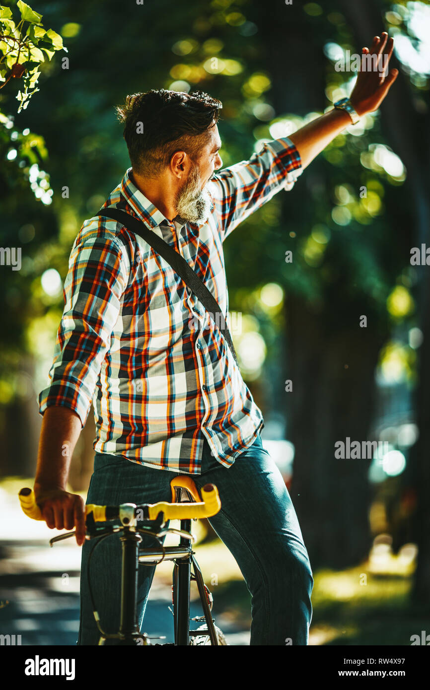 Ein hübscher junger Mann geht in die Stadt fahren mit dem Fahrrad, Sitzen, und winkte mit jemandem. Stockfoto