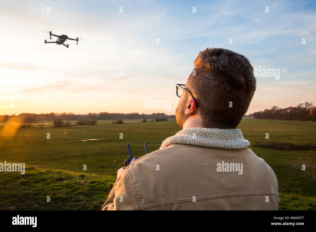 Ein über die Schulter geschossen von einem männlichen drone Pilot schweben und fliegen sein Drone auf eine sichere und verantwortungsvolle Art und Weise während draußen bei Sonnenuntergang Stockfoto