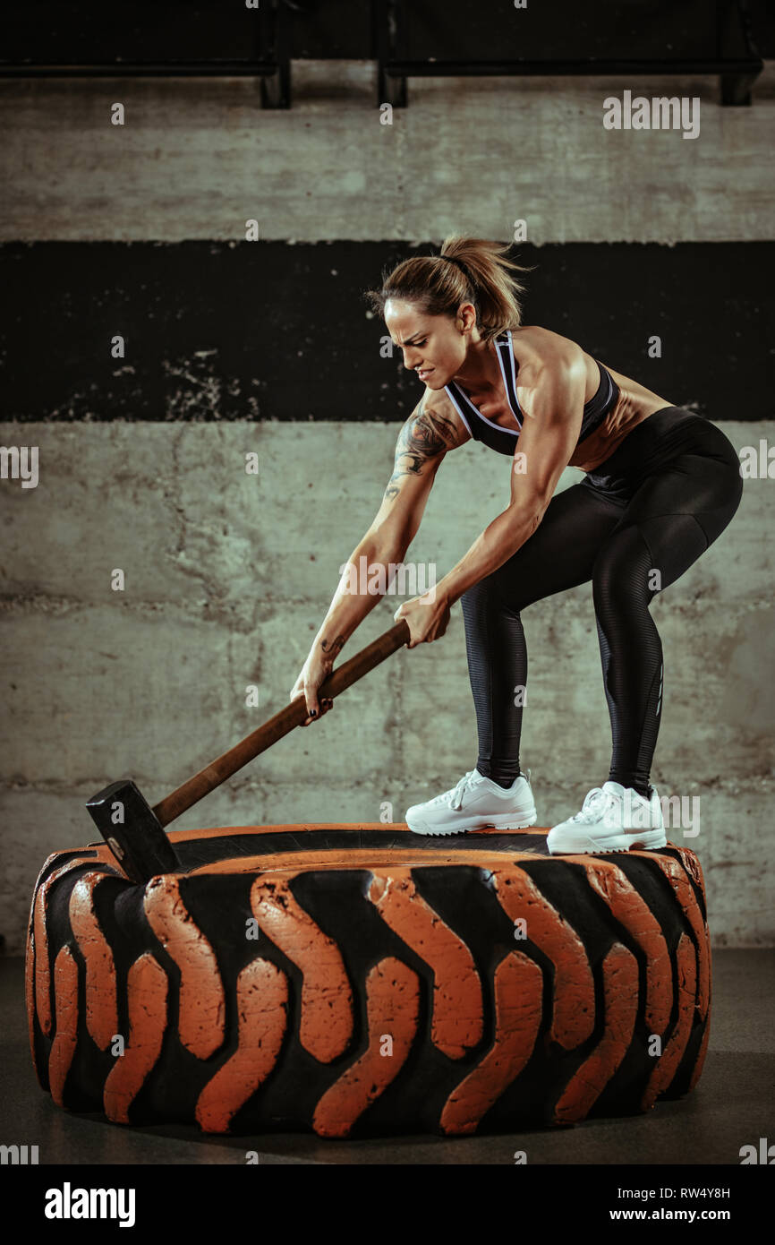 Junge muskulöse Frau schlagen Rad Reifen mit einem Hammer auf Training im Fitnessstudio. Stockfoto