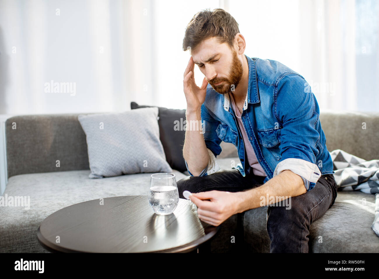 Mann trinken einige Arzneimittel schlechte Gefühl oder Kater nach der Alkohol Partei, sitzen auf der Couch zu Hause Stockfoto