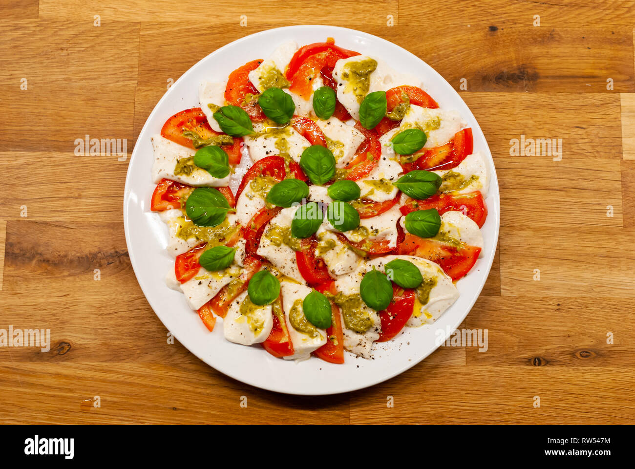 Blick von oben auf die Platte voll mit veganen Mozzarella von Cashew-nüssen mit Tomatenscheiben, Basilikum und Pesto auf einen hölzernen Tisch Stockfoto