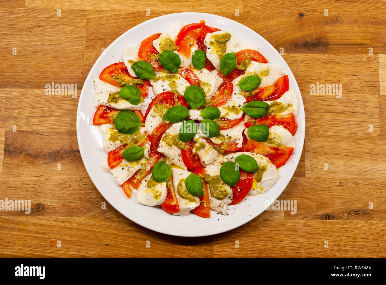 Blick von oben auf die Platte voll mit veganen Mozzarella von Cashew-nüssen mit Tomatenscheiben, Basilikum und Pesto auf einen hölzernen Tisch Stockfoto