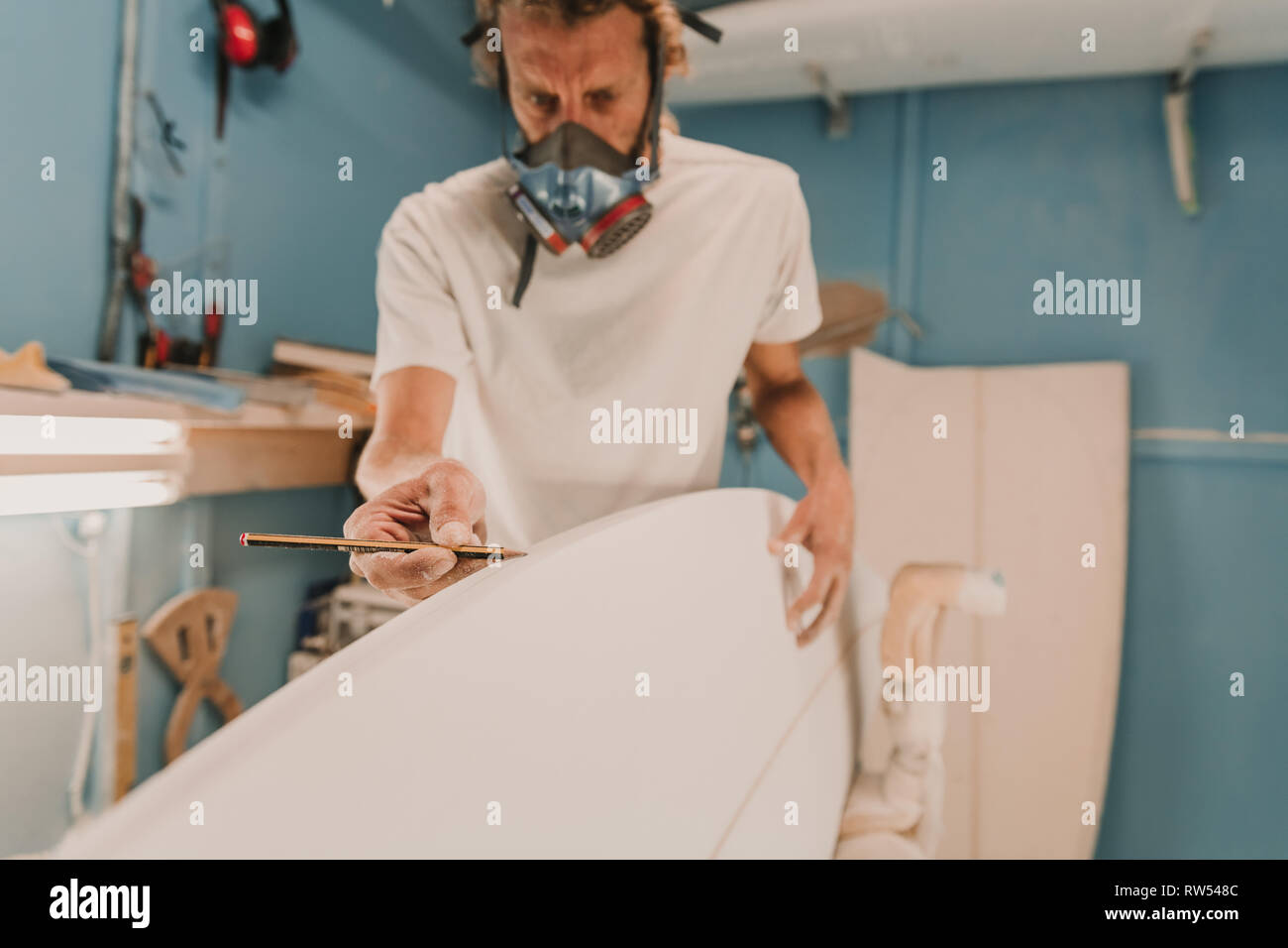 Mann in Atemschutzmaske Messung Surfbrett in der Werkstatt Stockfoto