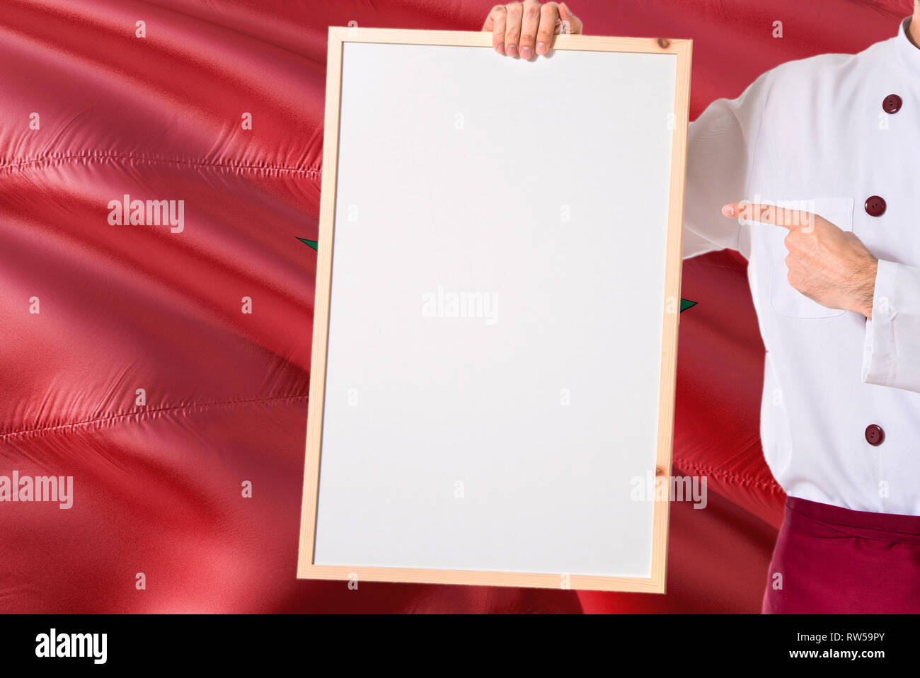 Marokkanische Koch Holding leeres Whiteboard Menü auf Marokko Flagge Hintergrund. Cook tragen einheitliche zeigt Platz für Text. Stockfoto