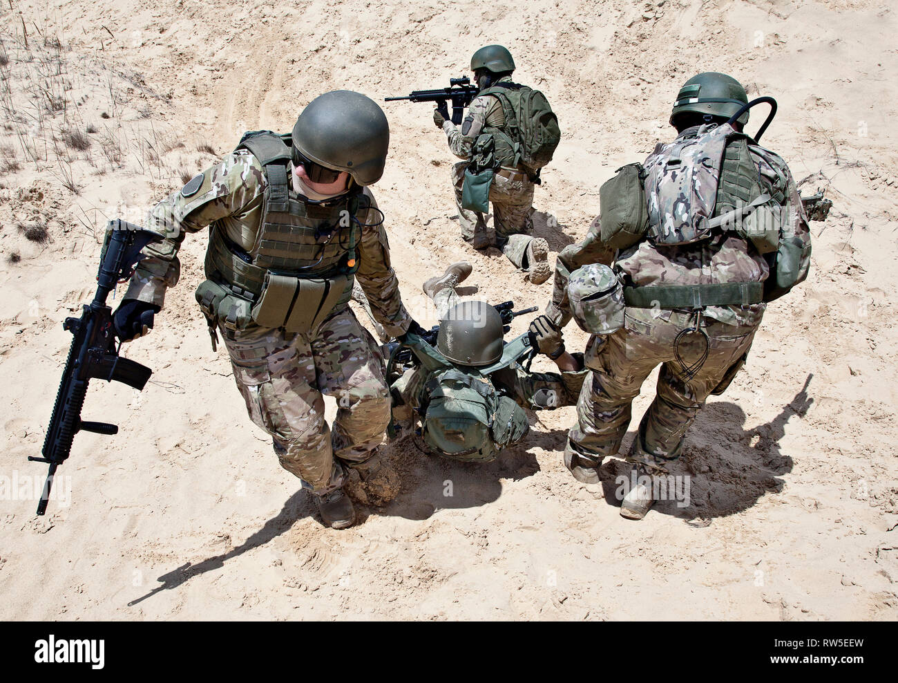 Trupp Soldaten evakuieren die verletzten Kollegen in den Armen, in der Wüste. Stockfoto