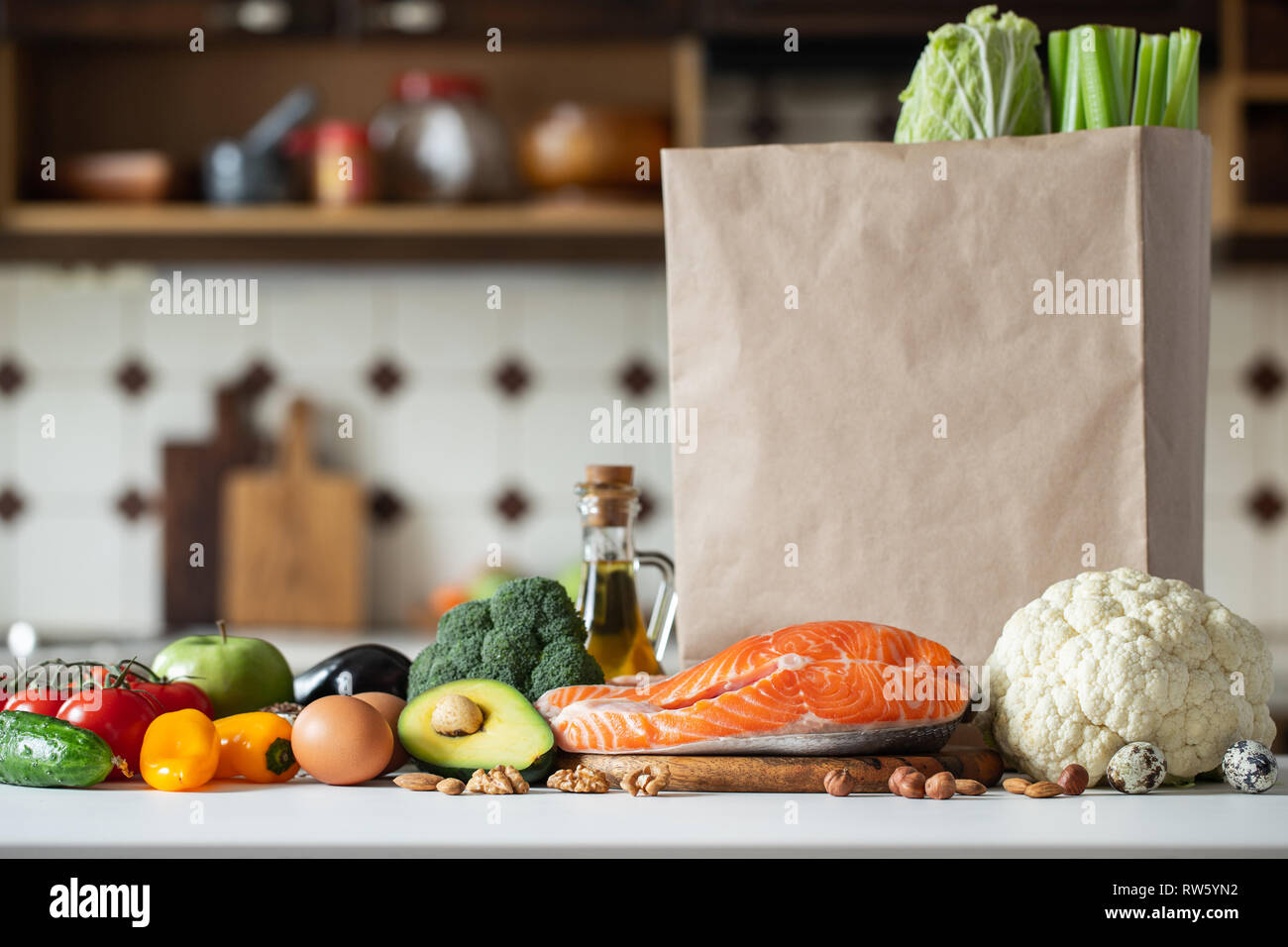 Frisches Gemüse, Früchte, Nüsse und Lachssteak auf dem Küchentisch neben einem leeren Papier Shopping Bag. Das Konzept der gesunden Ernährung und keto Diät. C Stockfoto