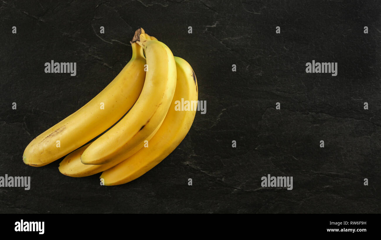 Von oben nach unten anzeigen, Bündel gelbe Bananen auf Schwarzes Brett, Platz für Text auf der rechten Seite. Stockfoto