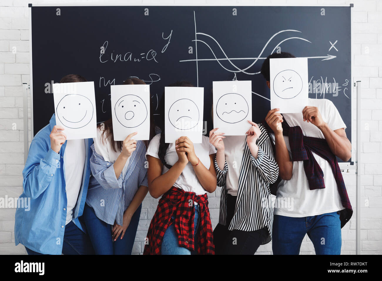 Studenten, die Gesichter mit Papieren über Tafel Stockfoto