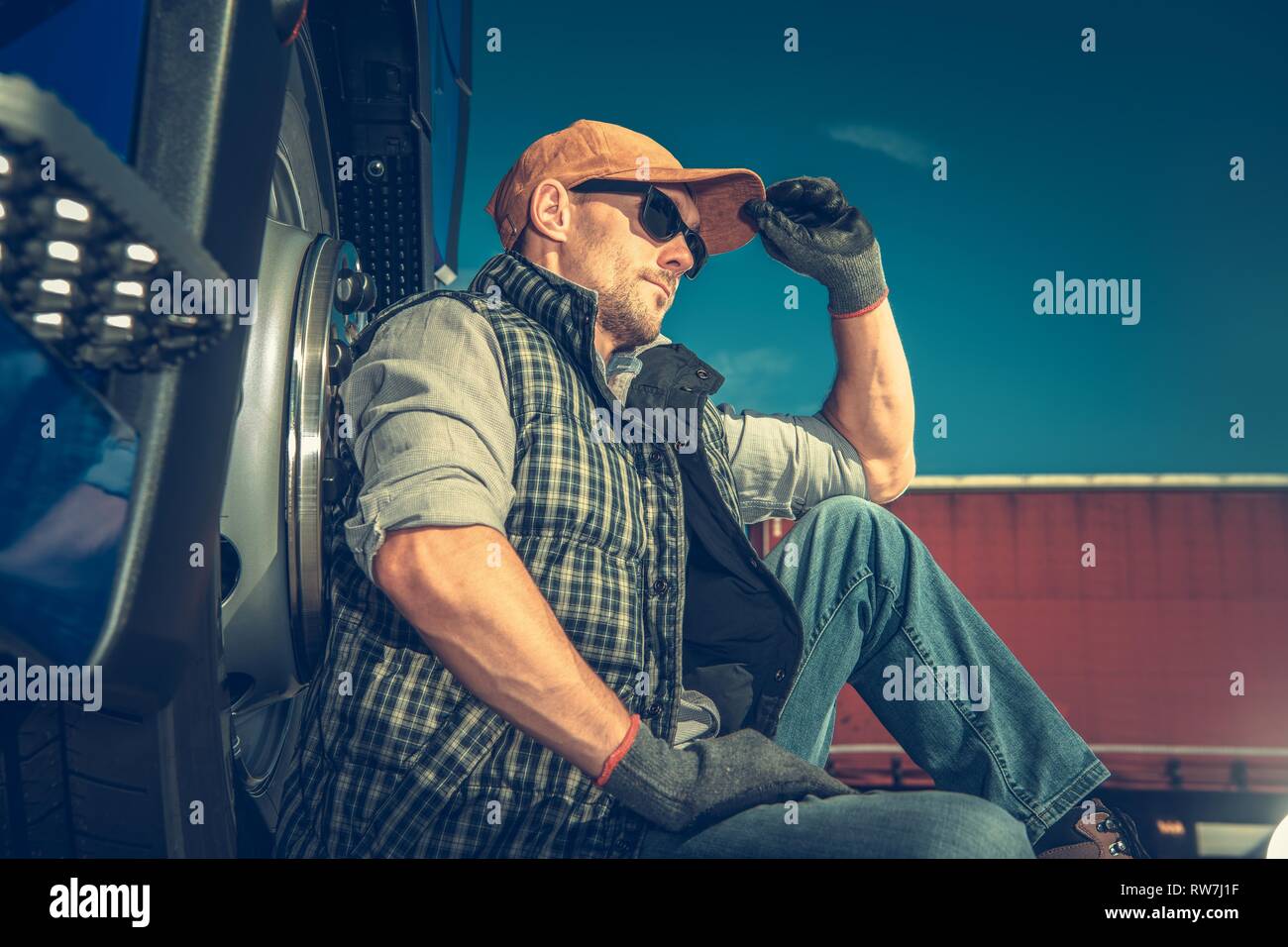 Halb LKW-Fahrer brechen. Transport schwerer Lasten. Kaukasische Trucker seine Rückseite auf einem Lkw-Rad auf den Bürgersteig zu unterstützen. Stockfoto