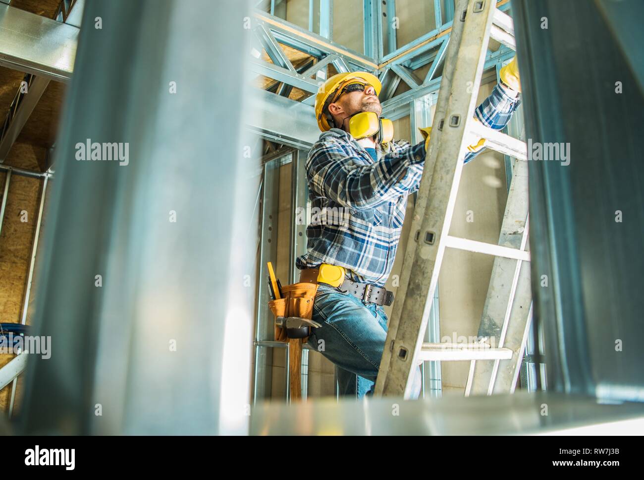 Skelett aus Stahl Bau Arbeiter tragen, Hart, Hut und Kopfhörer mit Geräuschreduzierung. Gehen mit Leiter. Stockfoto