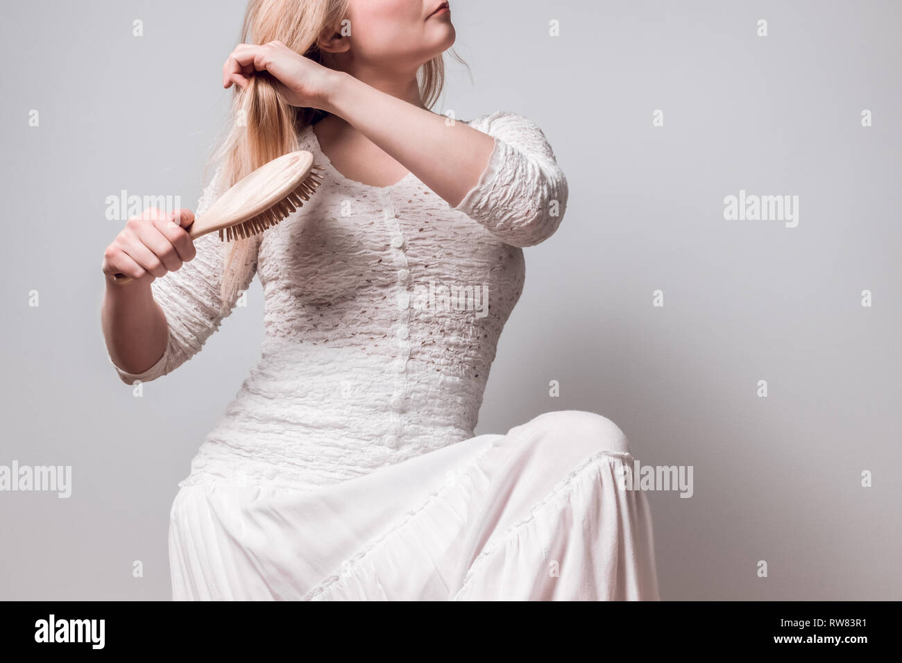 Junge Frau in weiß ihre langen blonden Haare bürsten mit einem hölzernen Haarbürste. Stockfoto