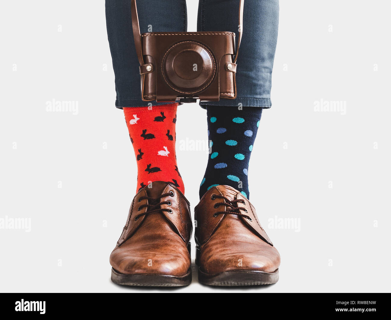 Männer Beine, schicke Schuhe, blaue Hosen, farbenfrohe Socken und vintage  Kamera in einer Ledertasche auf einem weißen Hintergrund, isoliert.  Close-up. Konzept der Stil Stockfotografie - Alamy