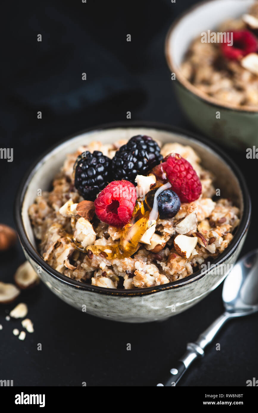 Schüssel Haferbrei Porridge mit Nüssen und Beeren auf schwarzem Hintergrund. Gesunde vegane oder vegetarische Kost Stockfoto