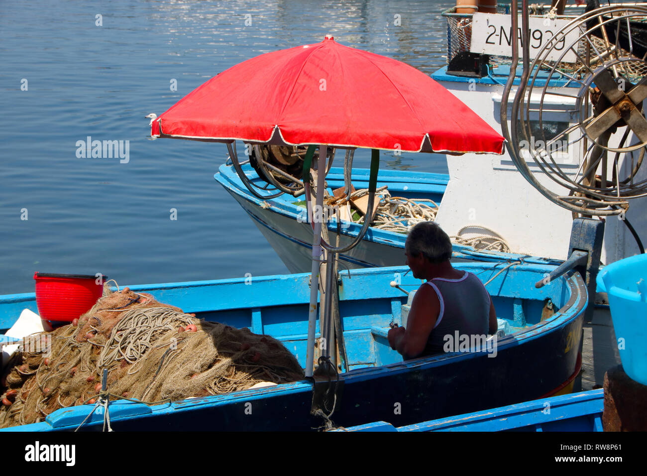 Bei Pozzuoli, Italien, Juni, 04/2018 - alten Fischer in seinem blauen Boot mit einem roten Regenschirm im Sommer Stockfoto