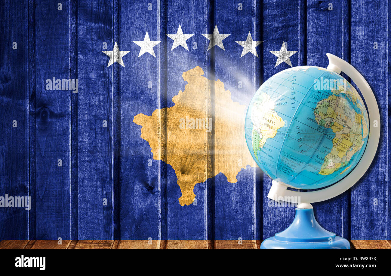 Globus mit einer Weltkarte auf einem hölzernen Hintergrund mit dem Bild von der Flagge des Kosovo. Das Konzept der Reisen und Freizeit im Ausland. Stockfoto