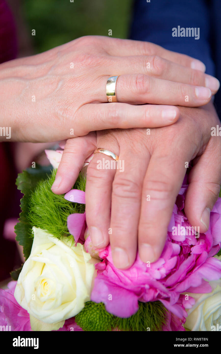Hände von Braut und Bräutigam mit Blumenstrauß und Trauringe Stockfoto