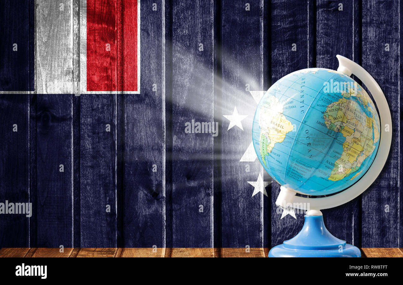 Globus mit einer Weltkarte auf einem hölzernen Hintergrund mit dem Bild der Flagge der Französischen Süd- und Antarktisgebiete. Das Konzept der Reisen und Freizeit abr Stockfoto